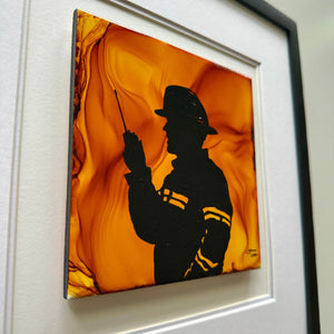 A square framed canvas art print featuring a black silhouette of a firefighter against a vibrant orange and yellow marbled background, mounted on a white textured wall.